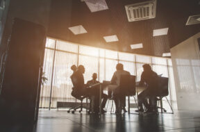 Silhouettes of people sitting at the table. A team of young businessmen working and communicating together in an office. Corporate businessteam and manager in a meeting